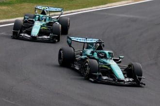 Aston Martin F1 aracı pistte yarışırken, arka planda takım çalışanları görülüyor.
