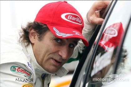 Alex Zanardi, yarış arabasında, zafer kazanmış şekilde gülümsüyor.