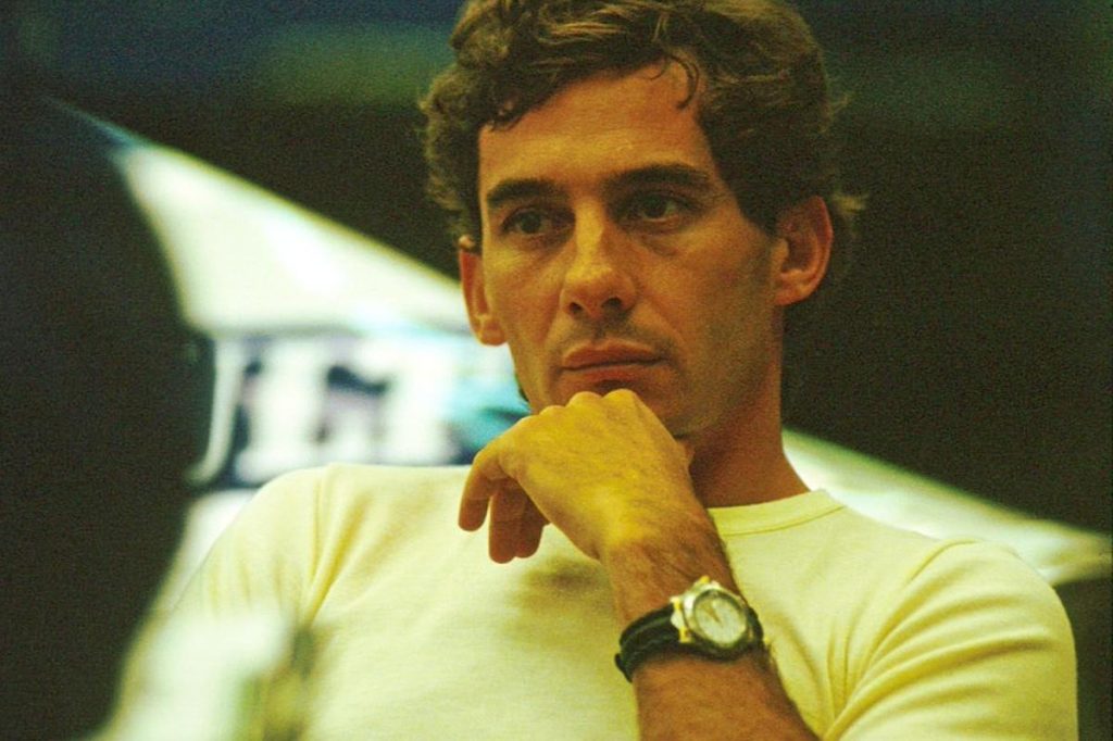 Ayrton Senna beyaz tisort paddockta dusunceli candid portre - Rolex saat bilekliginde, insani ve sakin bir an