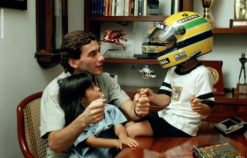 Ayrton Senna evinde iki cocukla oynarken - cocugun basinda Nacional BOSS Honda kasklı - kupa ve FIA plaket arkada - Norio Koike Resmi Senna Arsivi ASE2024