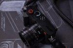 Leica Q3 43 Formula 1 Edition — F1 araç tasarım eskizleri üzerinde kamera, kırmızı deklanşör butonu, karbon fiber başparmak desteği ve örgülü F1 kayışı