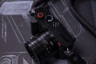 Leica Q3 43 Formula 1 Edition — F1 araç tasarım eskizleri üzerinde kamera, kırmızı deklanşör butonu, karbon fiber başparmak desteği ve örgülü F1 kayışı